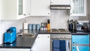 A modern kitchen with white cabinets, a blue refrigerator, a black countertop, and a stainless steel sink. - No. 33 Apartment 4, Hunstanton, Norfolk (Hunstanton)