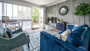 A living room with a blue sofa, a green armchair, a small table, and a TV. - No. 33 Apartment 4, Hunstanton, Norfolk (Hunstanton)