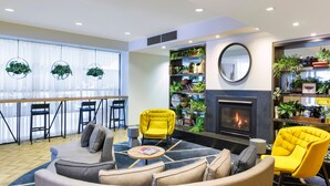 Ein modernes Wohnzimmer mit Kamin, gelben Sesseln, einem grauen Sofa und einem Bücherregal voller Pflanzen und Büchern.