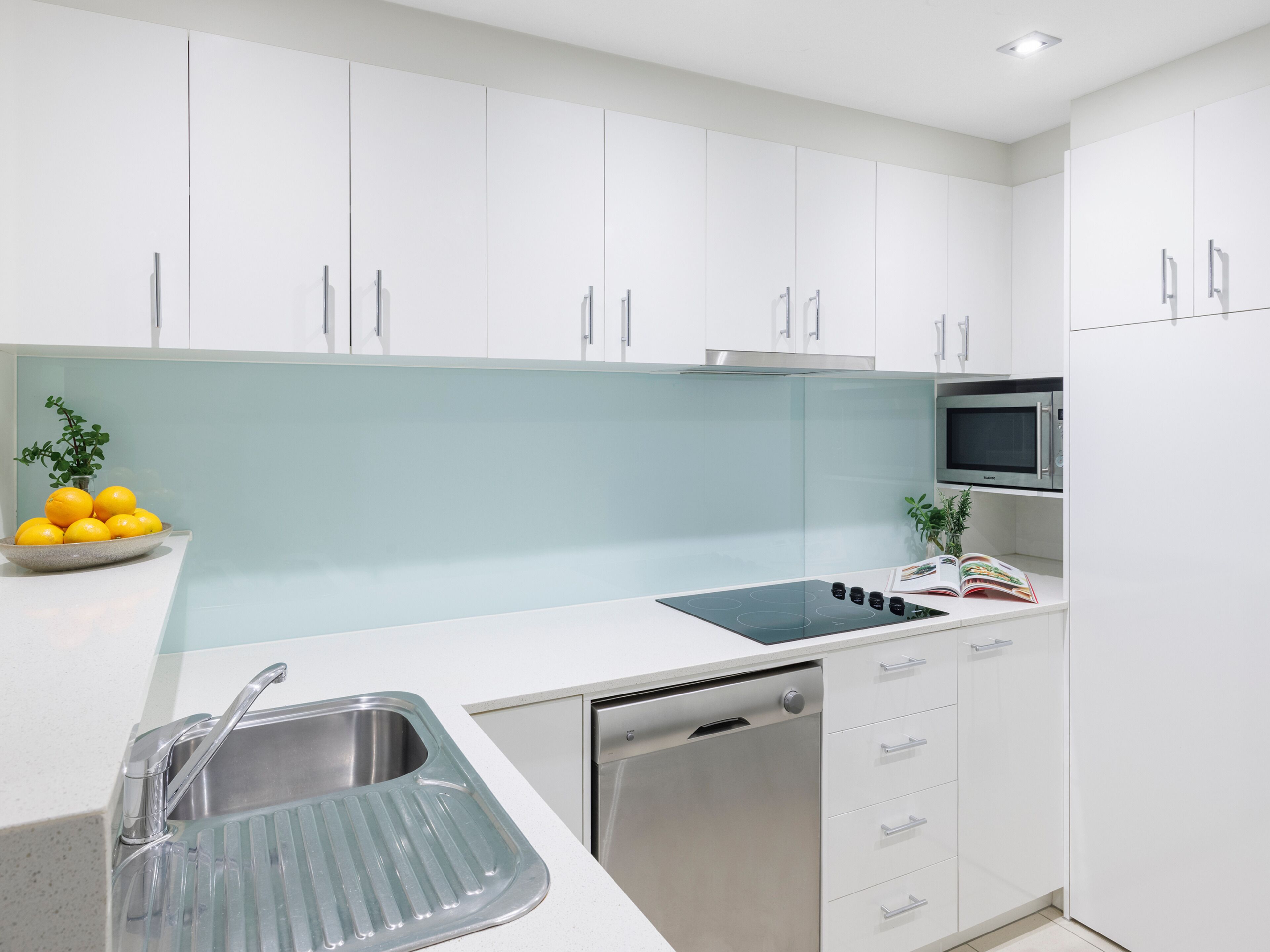 A modern kitchen with white cabinets, a stainless steel sink, a built-in microwave, and a dish rack.