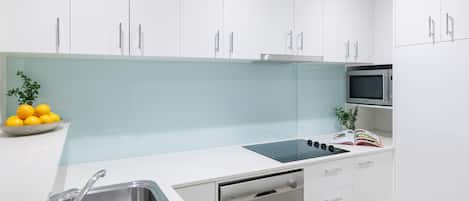 A modern kitchen with white cabinets, a stainless steel sink, a built-in microwave, and a dish rack.