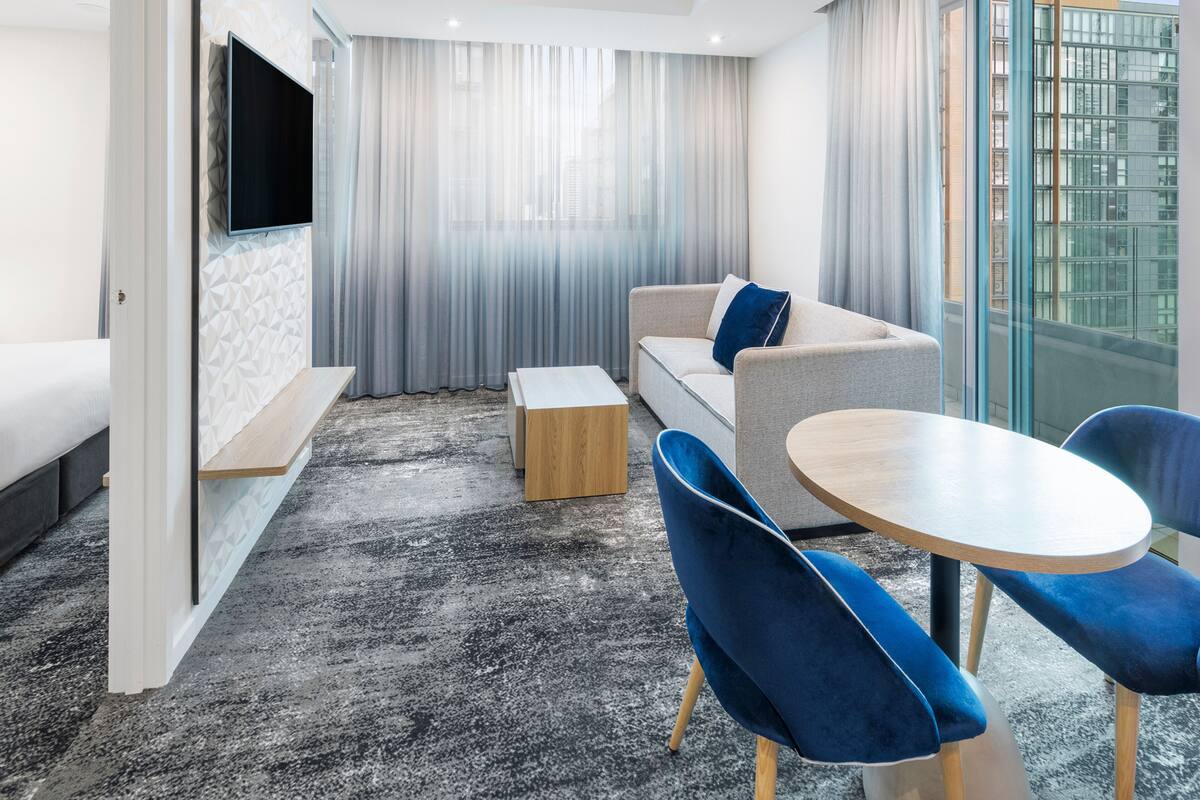 Una habitación de hotel moderna con una cama, un sofá, una mesita y un televisor montado en la pared.