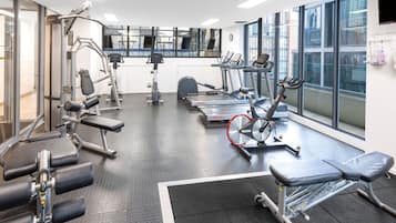 Un gimnasio con máquinas de cardio, estaciones de pesas y un espejo grande.