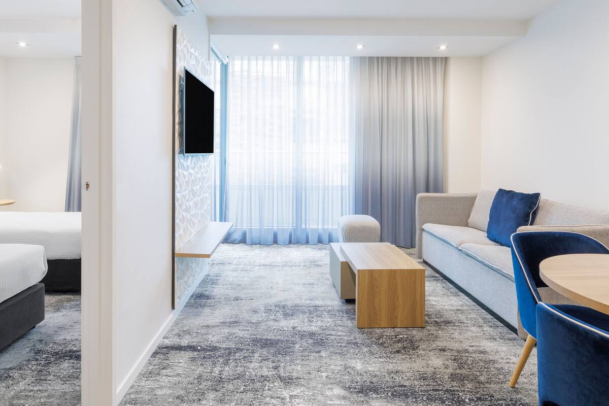 Una habitación de hotel moderna con cama, sofá, mesa de centro y televisor.
