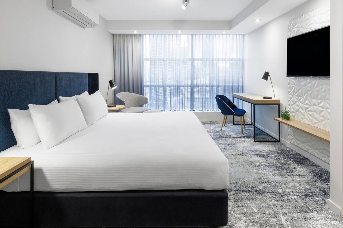Una habitación de hotel moderna con una cama grande, un escritorio, una silla y un televisor montado en la pared.