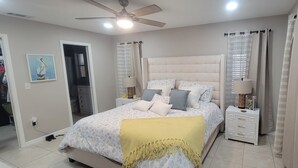 Ein Schlafzimmer mit Bett, Nachttischen, Deckenventilator und Vorhängen.