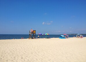 Een strand met een bewakerspost, parasols en mensen die ontspannen.