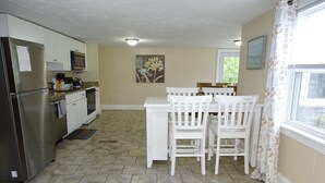 A kitchen with white cabinets, a stainless steel refrigerator, a microwave, and a dining area with white chairs and a table. - Beach family gateway, modern 5BR, walk to the beach, big yard, firepit (Dennis)