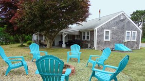 A house with a covered patio area featuring four turquoise Adirondack chairs arranged in a semi-circle. - Beach family gateway, modern 5BR, walk to the beach, big yard, firepit (Dennis)