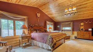 Un dormitorio acogedor con techo de madera, una cama grande con colcha estampada, dos lámparas de noche y un aparador.