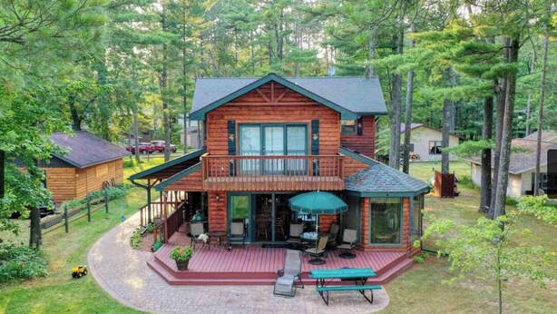 Una cabaña de troncos con terraza, mobiliario exterior y un ventanal grande con vistas a un bosque.
