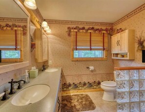 A bathroom with two sinks, a toilet, and a window with blinds.