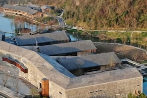 A modern building with a curved roof, a swimming pool, and a forested hillside in the background. - Hangzhou Denver Countryside Hotel (Agriculture and Forestry University) (Hangzhou)