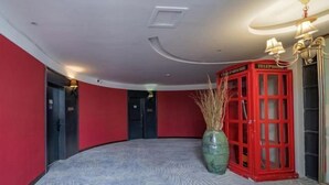 Una habitación con un teléfono rojo, un florero verde con plantas secas y un suelo estampado.