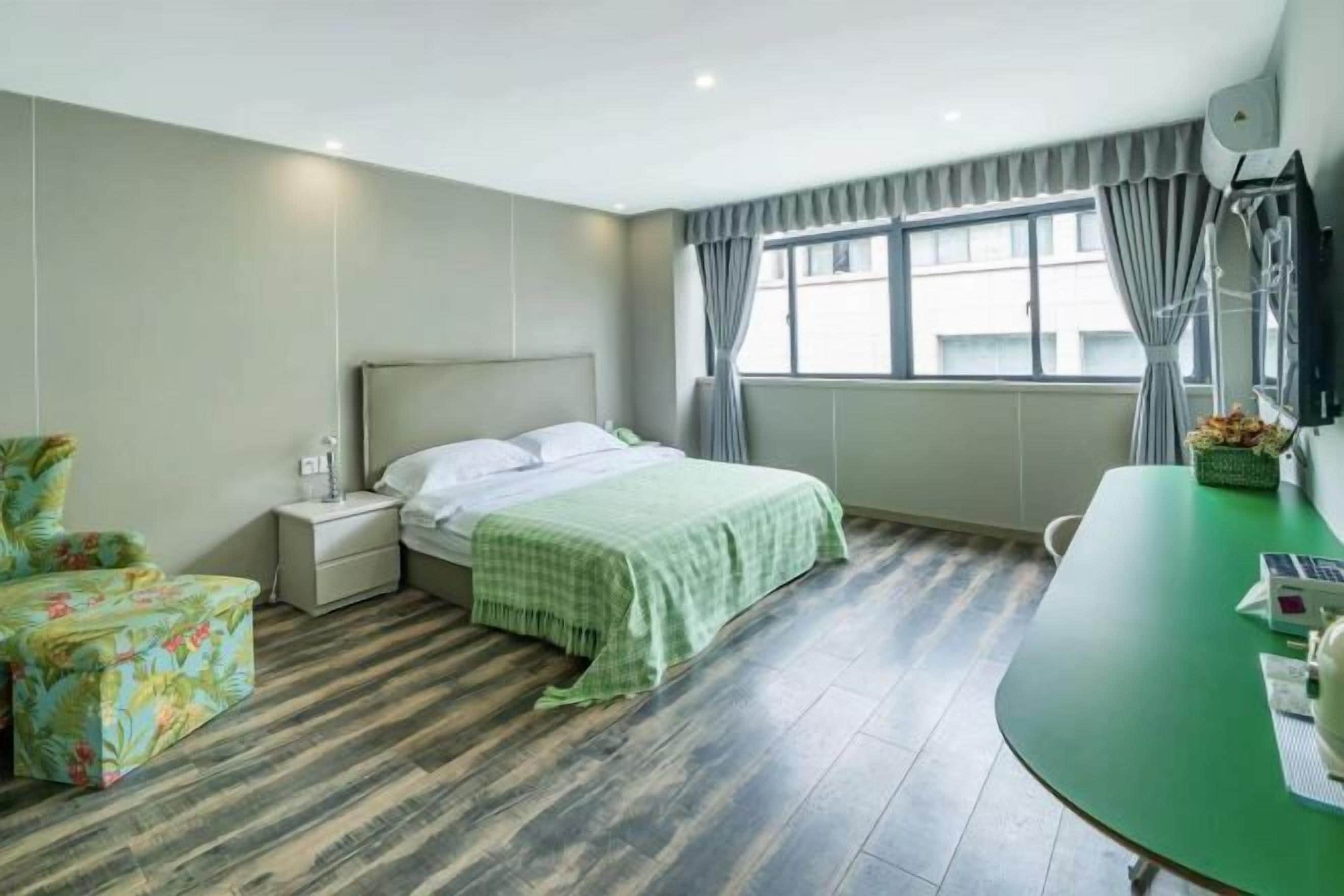 A hotel room with a bed, a nightstand, a chair, a table, and a window with curtains.
