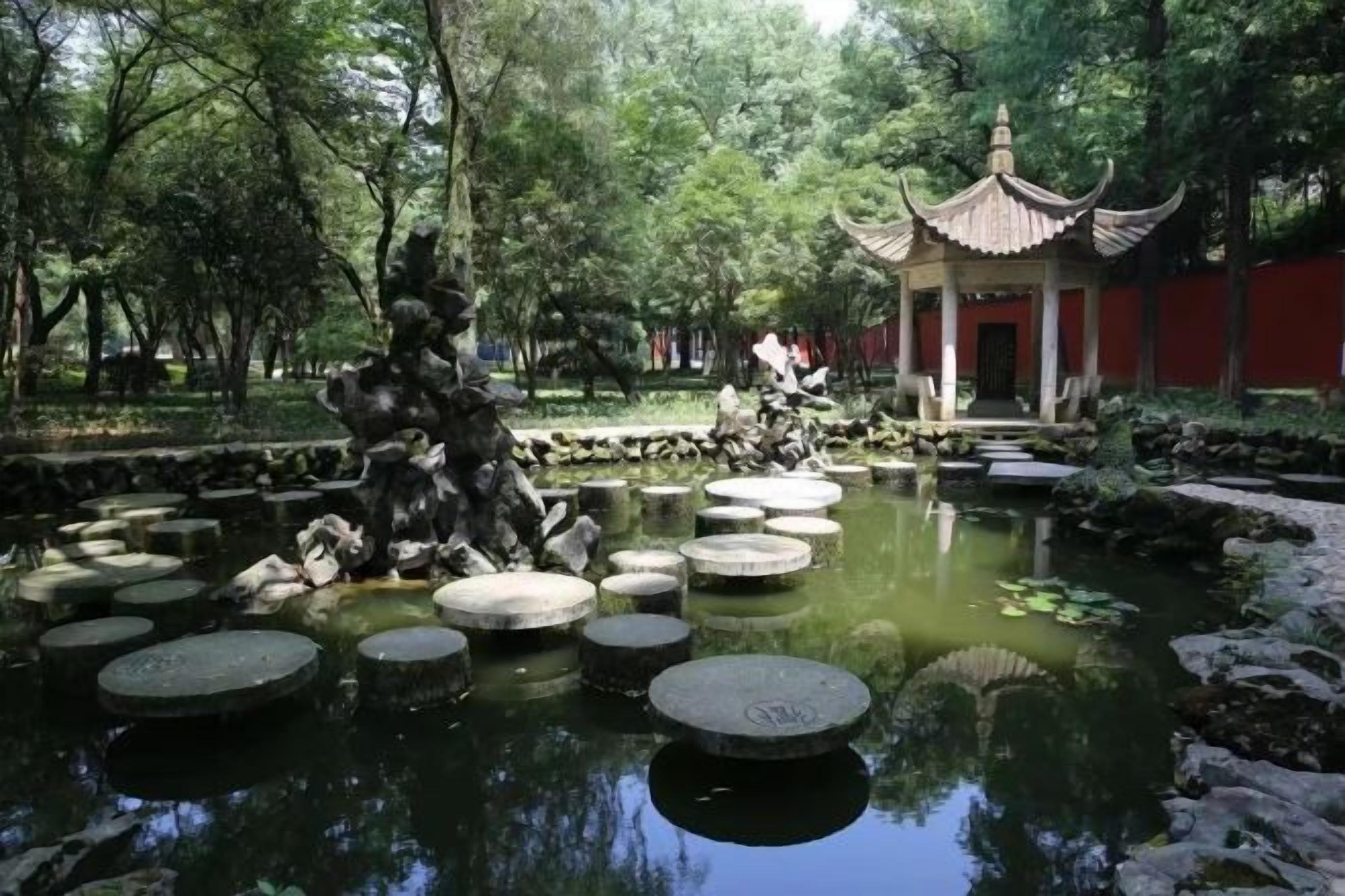 A traditional Chinese pavilion with a pond and stepping stones.