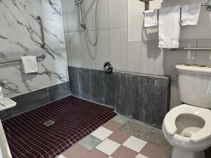 A bathroom with a shower, toilet, and a tiled floor. - Lanai Motel (Alhambra)