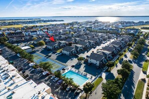 A residential area with a large swimming pool, multiple parking spaces, and a view of the sea.