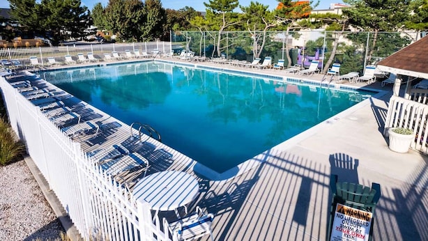 A rectangular swimming pool with a deck area, surrounded by a white fence and shaded by trees. - Renovated 1st Floor 2 Bedroom Condo close to pool and beach with outdoor space. (Ocean City)