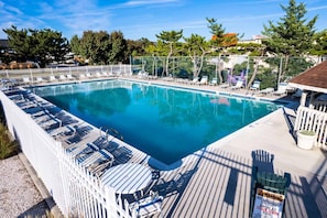 A rectangular swimming pool with a deck area, surrounded by a white fence and shaded by trees.