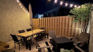 An outdoor patio with a wooden table and chairs, string lights, and a potted plant. - Renovated 1st Floor 2 Bedroom Condo close to pool and beach with outdoor space. (Ocean City)