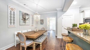 Un coin repas avec une table et des chaises en bois, un lustre et une cuisine dotée d’un comptoir-bar.