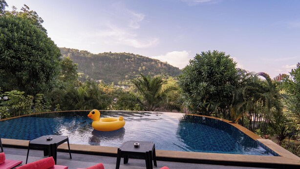 A pool with a yellow inflatable duck, red lounge chairs, and a view of a forested hill.