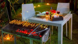 An outdoor dining area with a grill, chairs, a table set with wine glasses, a bottle, and a candle.