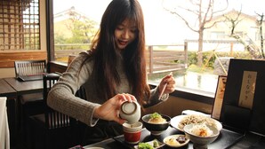 A person pouring tea into a cup at a table with bowls of food and a menu stand.