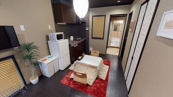 A compact kitchen with a microwave, refrigerator, and sink. There is a small dining area with a table and chairs. A potted plant and a red rug are visible.