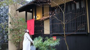 A traditional building with a wooden facade, a small garden with rocks and plants, and a red cloth hanging on the entrance.