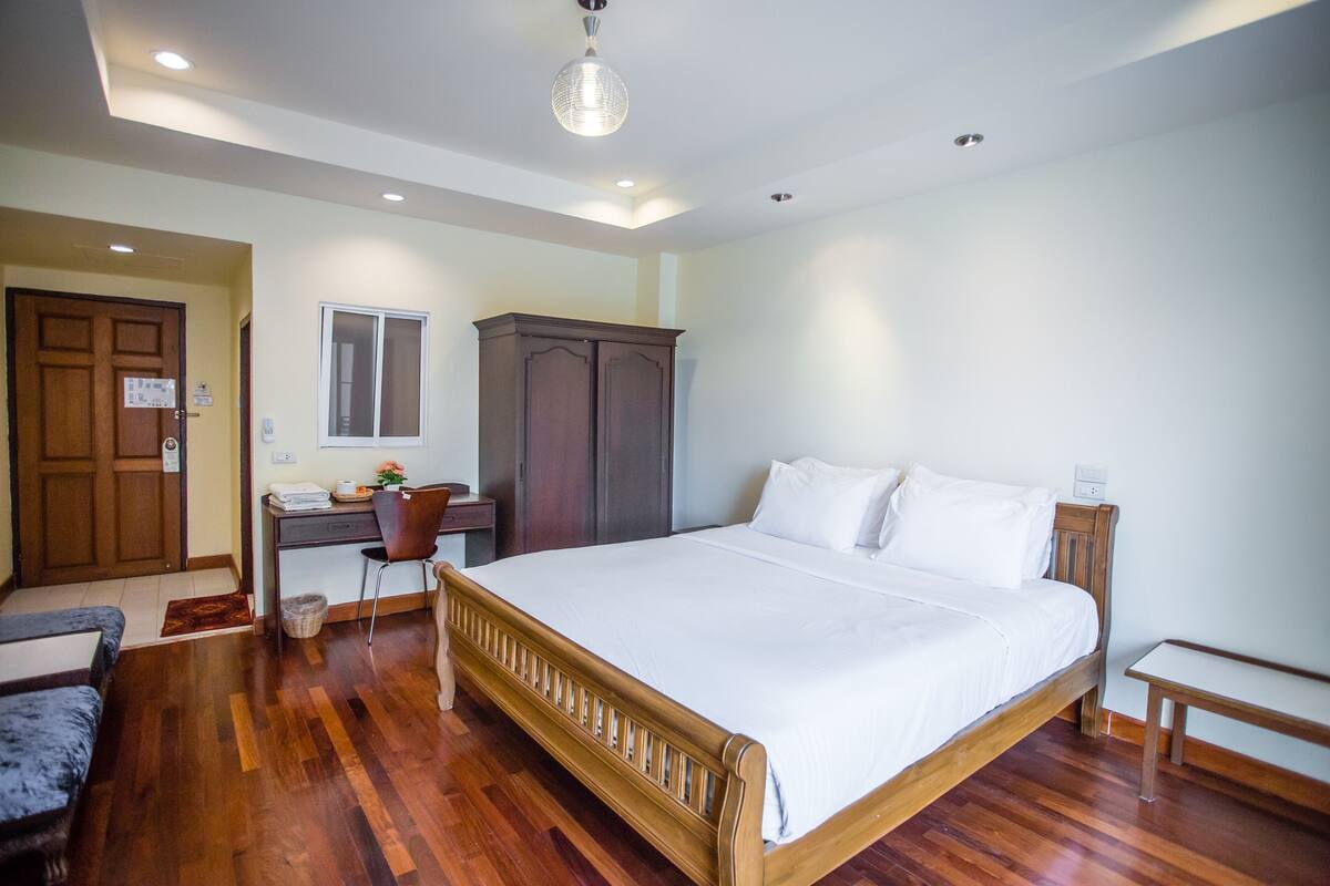 A bedroom with a wooden bed, a desk with a chair, a wardrobe, and a small table.