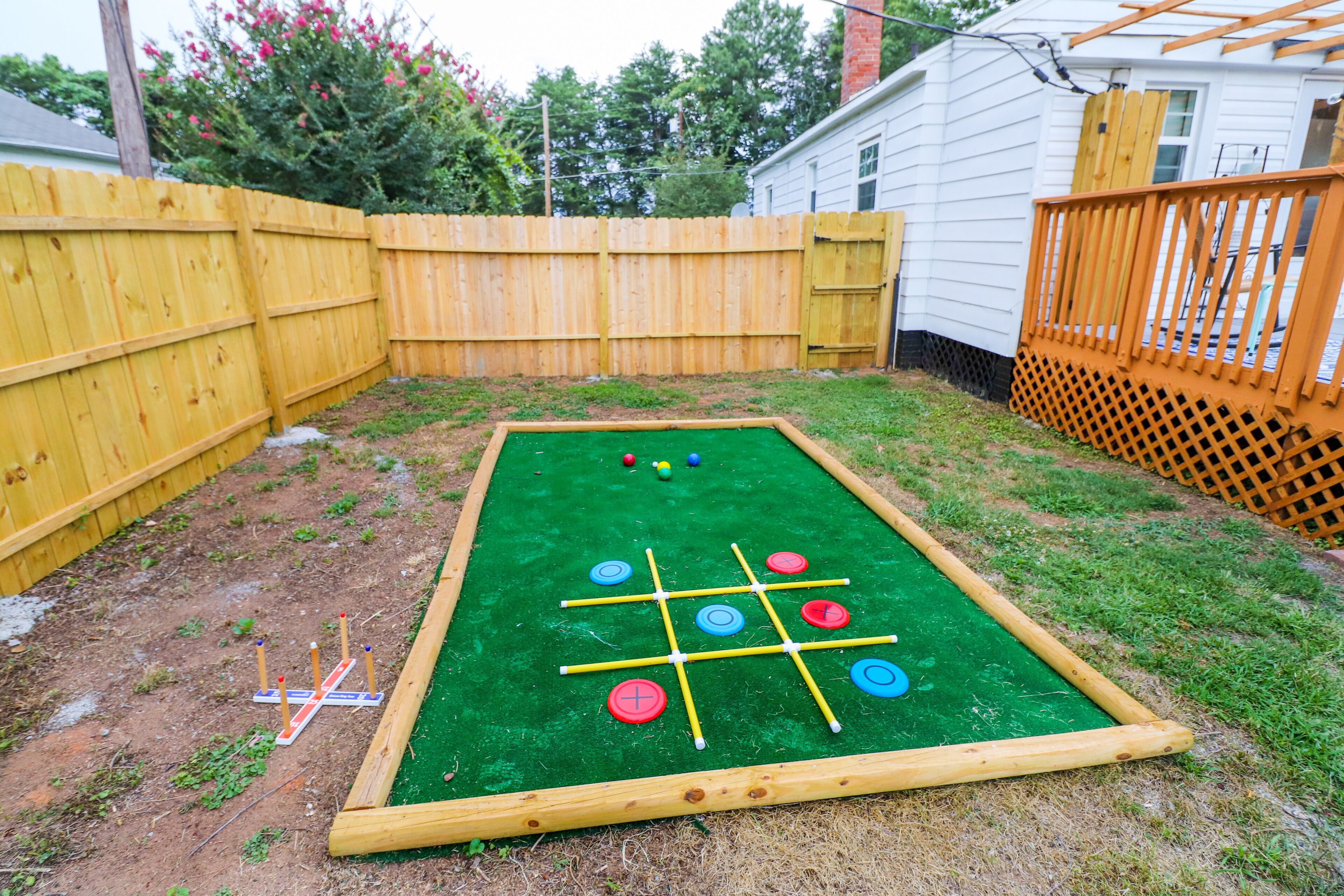 Une table de jeux d’extérieur verte, dotée d’un cadre en bois et d’un filet, entourée d’une clôture en bois et d’une terrasse en bois.
