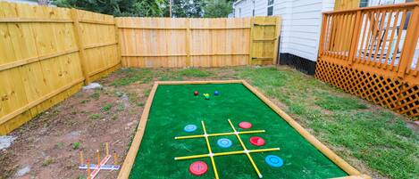 Une table de jeux d’extérieur verte, dotée d’un cadre en bois et d’un filet, entourée d’une clôture en bois et d’une terrasse en bois.