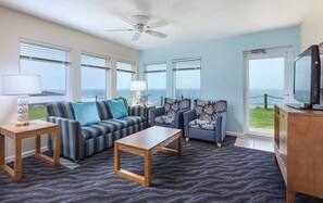 Relax in this stylish living room with a sofa, side table, lamp, coffee table, and TV, all set against a serene ocean view.