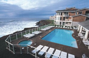 Relax by the resort's large pool, surrounded by lounge chairs and a hot tub, with ocean views from the multi-story building.
