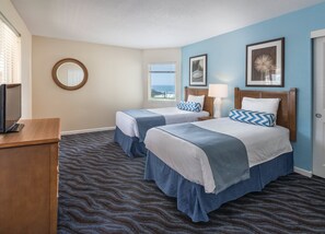 Two single beds with matching headboards and footboards, a wooden desk, and a large window offering an ocean view.