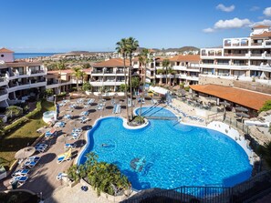 A resort with a large swimming pool, sun loungers, and a view of the ocean.