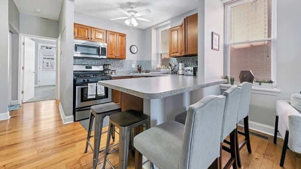 A modern kitchen with wooden cabinets, a central island, bar stools, and a ceiling fan. - 3 King Beds/3Baths Spacious by StayStLouis (St. Louis)