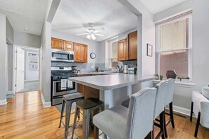 A modern kitchen with wooden cabinets, a central island, bar stools, and a ceiling fan.
