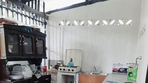 Una cucina compatta con fornello a gas, bollitore e lavandino. Si vede un pensile con cassetti e un piano di lavoro con un bollitore e una scatola.