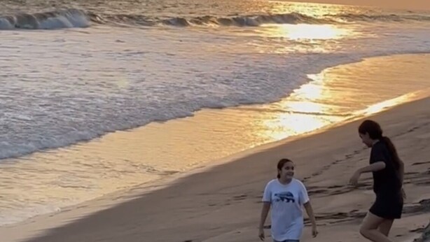 Una spiaggia al tramonto, con le onde e due persone che camminano lungo la riva.