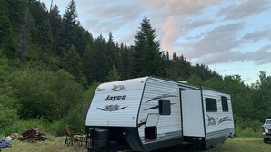 Un camper Jayco Rocky Mountain Edition parcheggiato in un'area erbosa con uno sfondo boschivo.