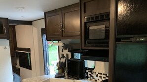 Una cucina compatta con mobili in legno scuro, piano cottura in acciaio inox, forno a microonde e frigorifero.