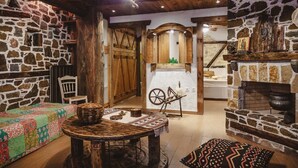 A rustic interior with stone walls, wooden beams, a stone fireplace, and a spinning wheel.