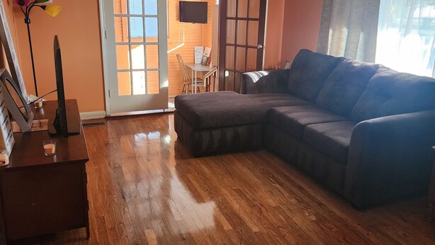 A living room with a sectional sofa, wooden flooring, a ceiling fan, and a sliding glass door leading to a balcony.