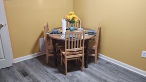 A dining area with a round table, four wooden chairs, a vase with yellow flowers, and a white paper towel holder.