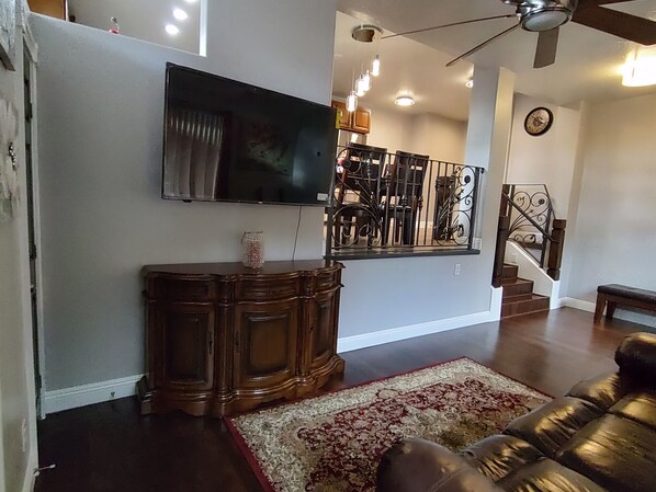 A living room with a flat-screen TV mounted on the wall, a wooden console table, a patterned rug, and a leather sofa. - The Queen's Respite (A) 2 bedrooms, 2 bathrooms (Toquerville)
