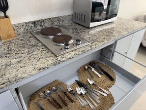 Cozinha com bancada de granito, micro-ondas e gaveta com utensílios.