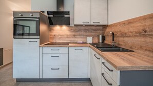 Una cocina moderna con horno empotrado, campana de acero inoxidable, salpicadero de madera y un lavamanos con grifo negro.